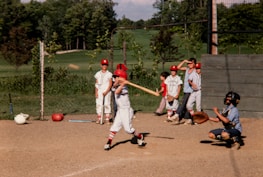 Volunteers from Asovembra helping children play baseball in a sunny park.
