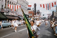Children and families attending a patriotic parade, waving small flags along a tree-lined street.