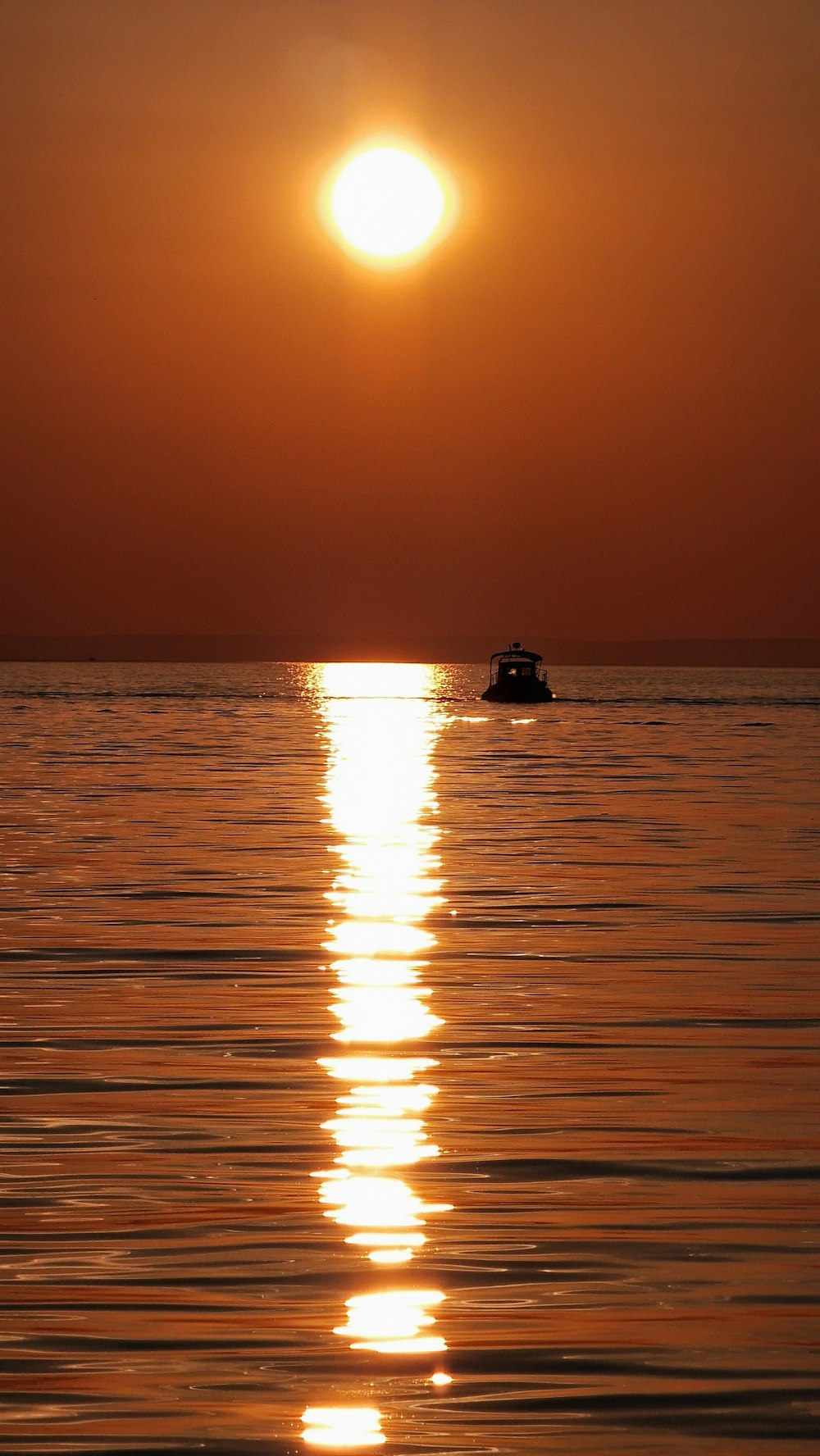 the sun is setting over the ocean with a boat in the water