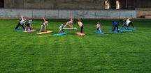 A small group practicing yoga on a wooden deck surrounded by lush greenery.