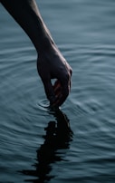 A hand gently touching ripples on the surface of a dark, still pond.