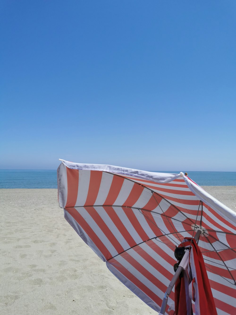 a red and white striped umbrella sitting on top of a sandy beach