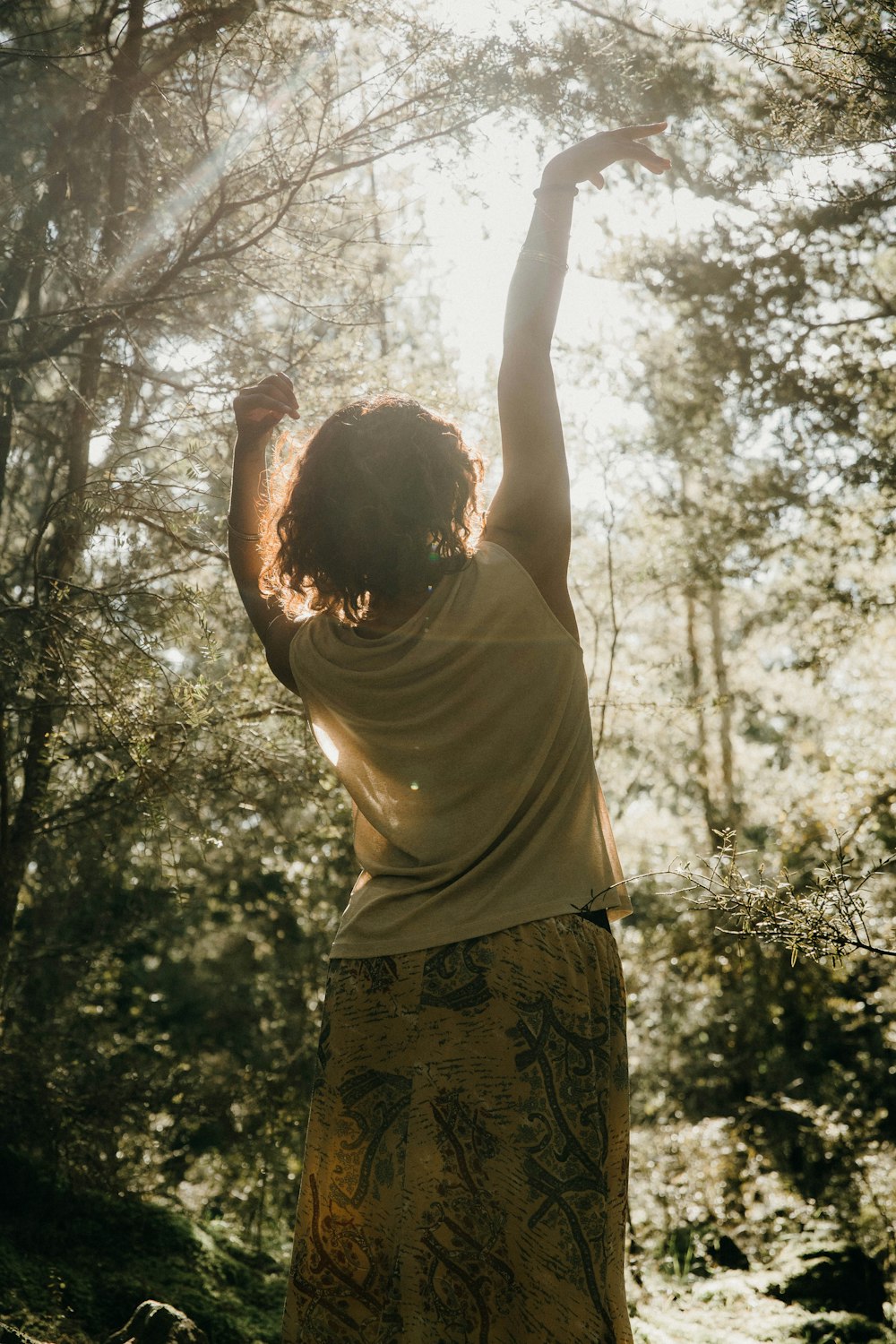 a woman standing in a forest reaching up into the sky