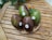 Several avocados with stickers are placed in a woven basket on a wooden table. The table is outdoors and surrounded by a few green leaves with small orange flowers.