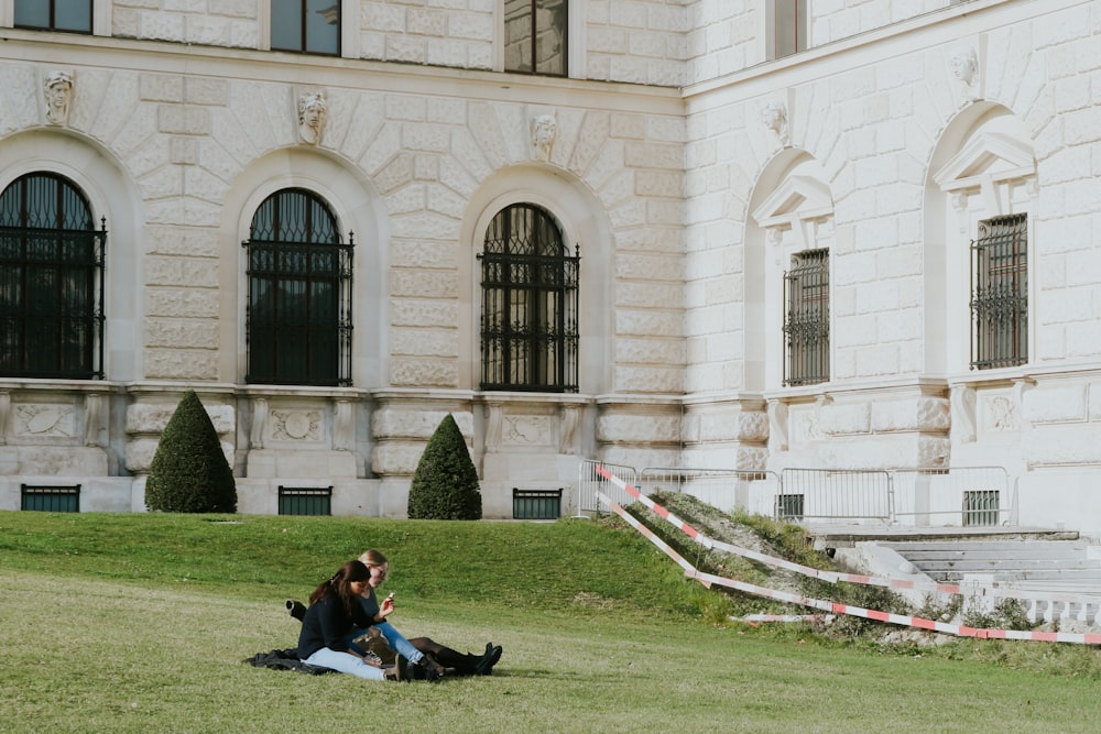 a man and woman sitting on the ground in front of a building