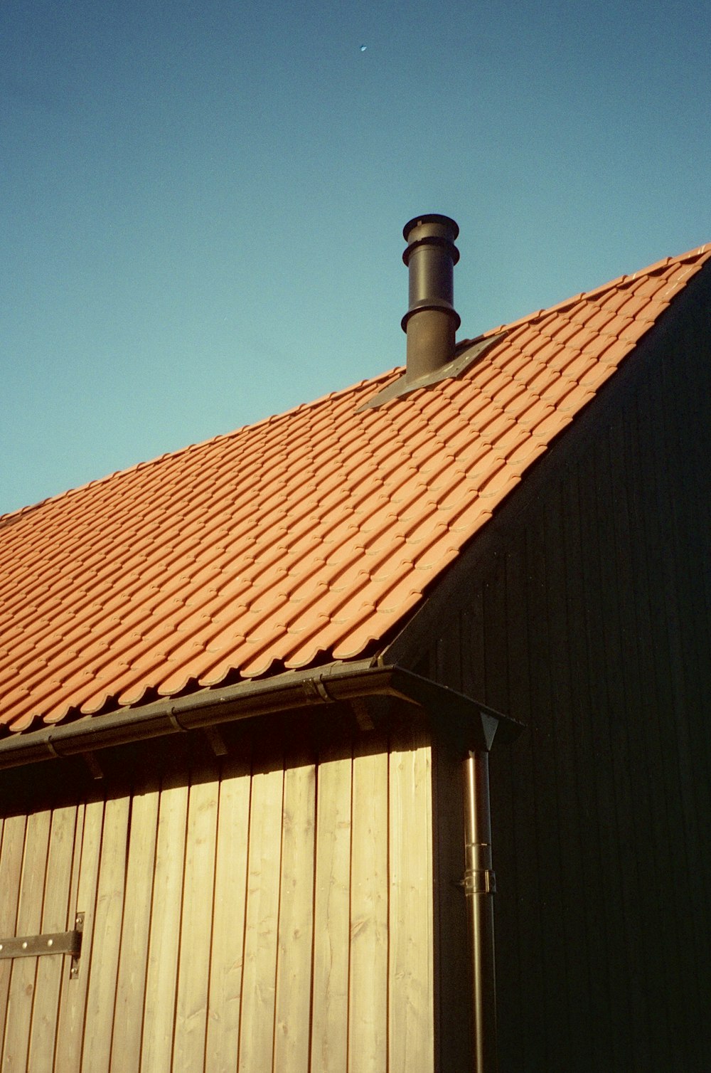a brown building with a red roof and a black chimney