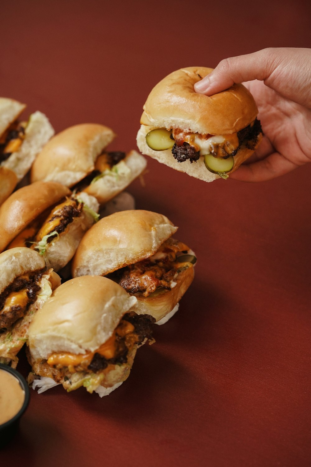 a hand holding a sandwich over a pile of mini sandwiches