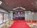 A red carpet leads to a backdrop with bright lights and the words in multiple languages, suggesting a cinematic or award-themed environment. Velvet ropes with gold stanchions line the carpet, and the adjacent wall features movie posters.