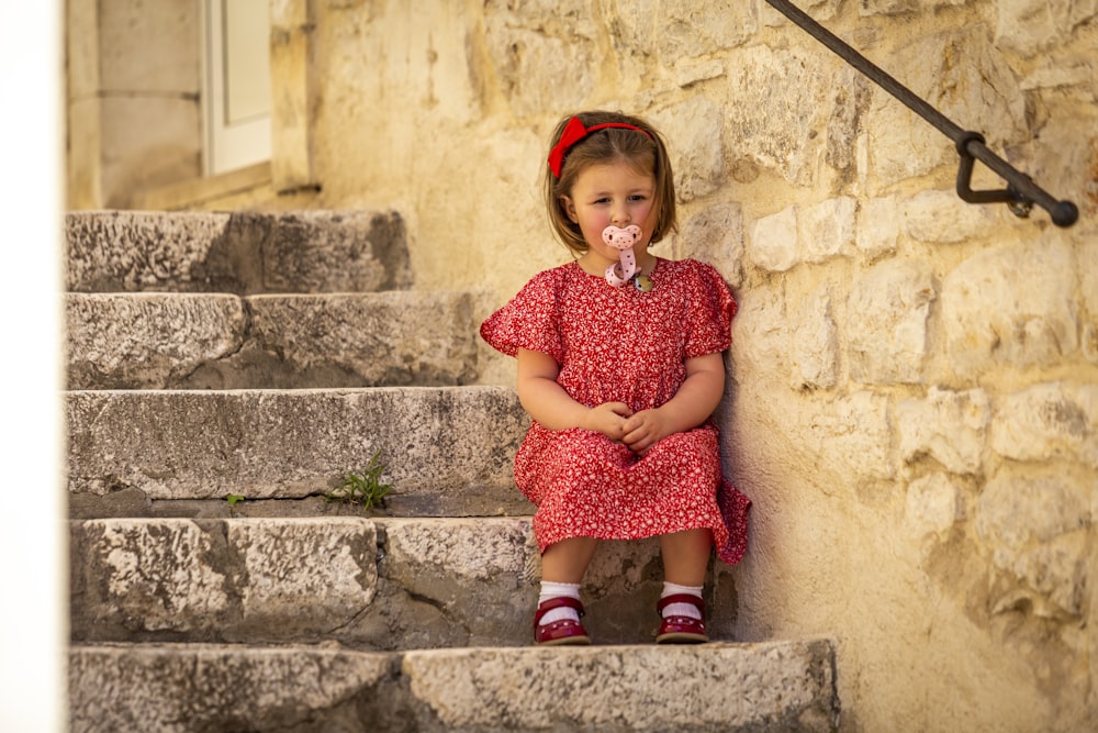 a little girl sitting on some steps with a pacifier in her mouth