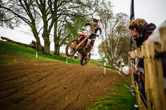 A dynamic motocross rider jumping over a dirt track in a lush green forest