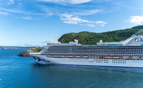 A luxury cruise ship cutting through crystal-clear aqua waters near tropical shores.