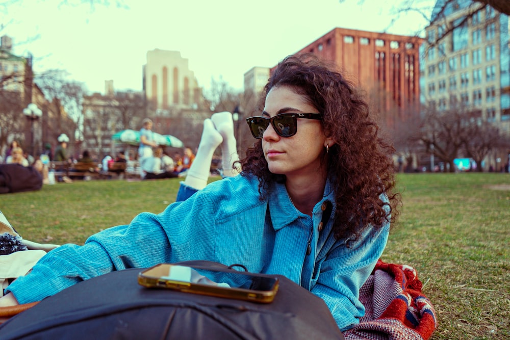 a woman sitting on the grass with a cell phone in her hand