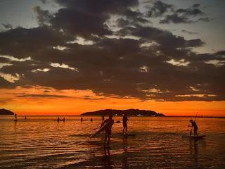 Guests paddleboarding on calm turquoise waters with a golden sunset backdrop.