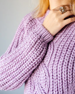 A stylish woman wearing layered zodiac rings, her hand resting on a soft cream-colored sweater.