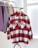 A red and white plaid button-up shirt is hanging on a clothes rack. Beside it are other garments in neutral tones like beige and purple. The setting is bright with a modern, minimalistic design.