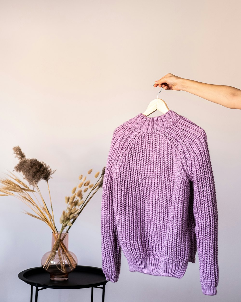 a purple sweater hanging on a rack next to a vase with dried flowers