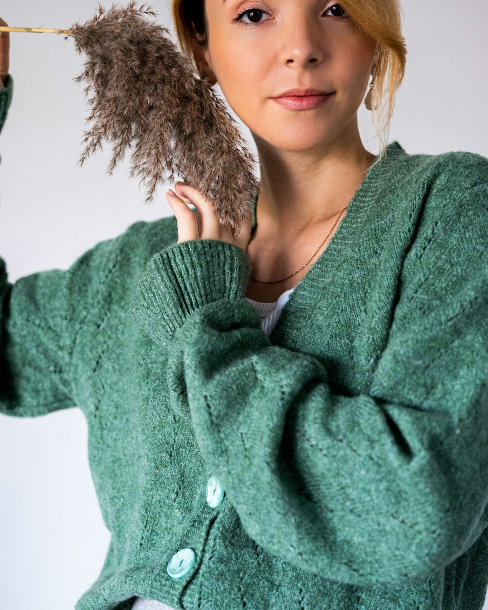 a woman in a green sweater holding a feather