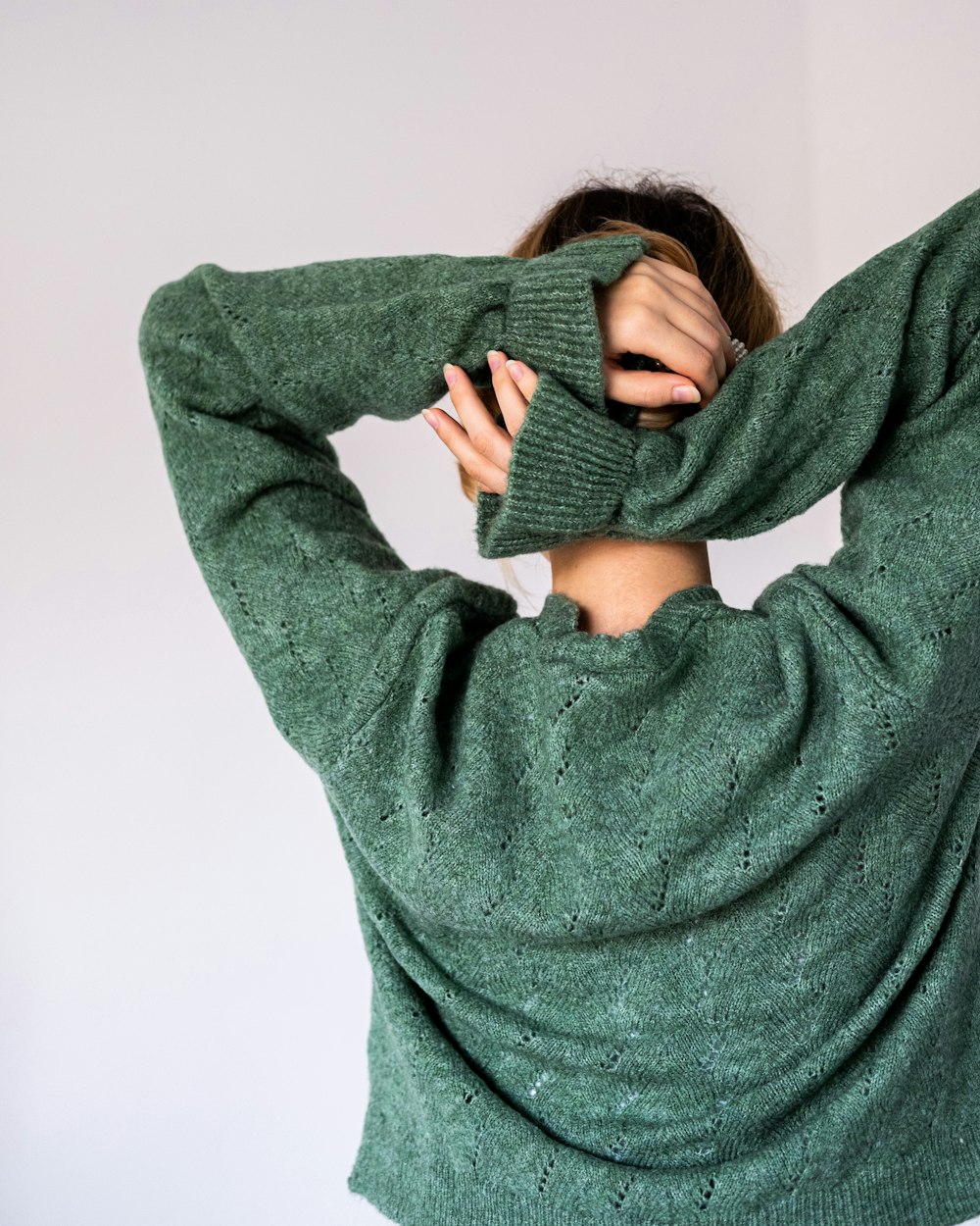 a woman in a green sweater covering her face with her hands