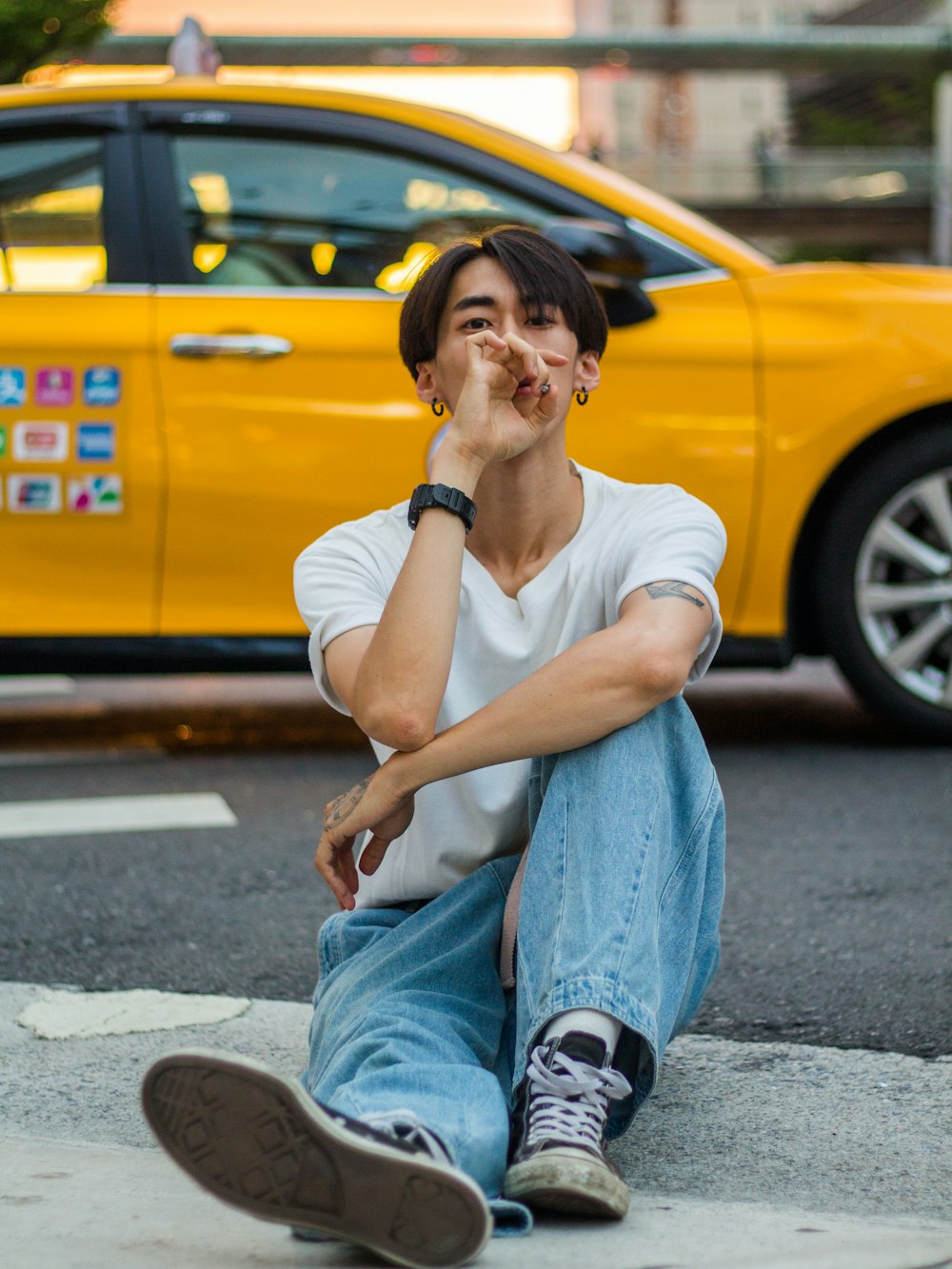 a young man sitting on the ground in front of a yellow taxi