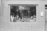 A brick wall features a large window display filled with various toys and apparel. Among the items are stuffed animals, figurines, and small decorative objects. The window sign indicates that the store sells books, toys, and apparel.