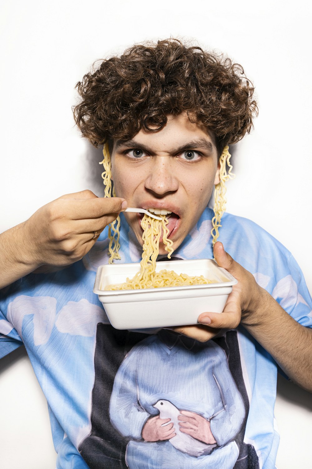 a man with curly hair eating a bowl of noodles