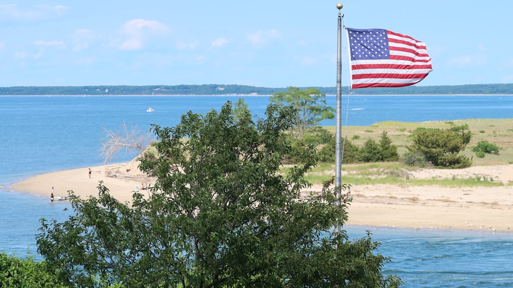 a large american flag flying over a beach next to a body of water