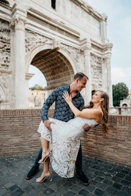 photography poses for couples,how to photograph man and woman at the roman forum, dip, dancing couple, dancing, couple in love, looking at each other, alecia sanfilippo and alex sanfilippo founder of podpros, podpros.com; a man holding a woman in front of an arch of triumph