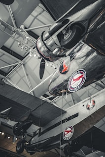 Several vintage airplanes are displayed in a museum setting with visible branding for American Airways and Douglas DC-3. The aircraft are suspended from the ceiling with visible structural elements, lighting fixtures, and metallic details.