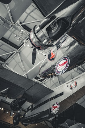 Several vintage airplanes are displayed in a museum setting with visible branding for American Airways and Douglas DC-3. The aircraft are suspended from the ceiling with visible structural elements, lighting fixtures, and metallic details.