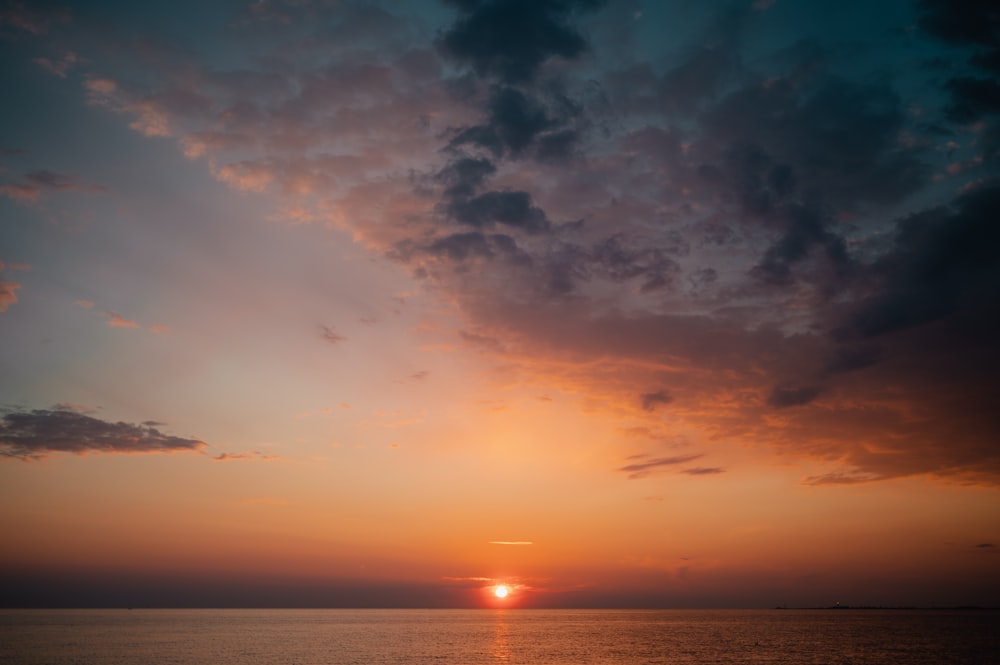 the sun is setting over the ocean on a cloudy day