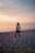 A joyful woman walking on a beach at sunset, dressed in marsala and pink hues.