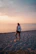 A joyful woman walking on a beach at sunset, dressed in marsala and pink hues.