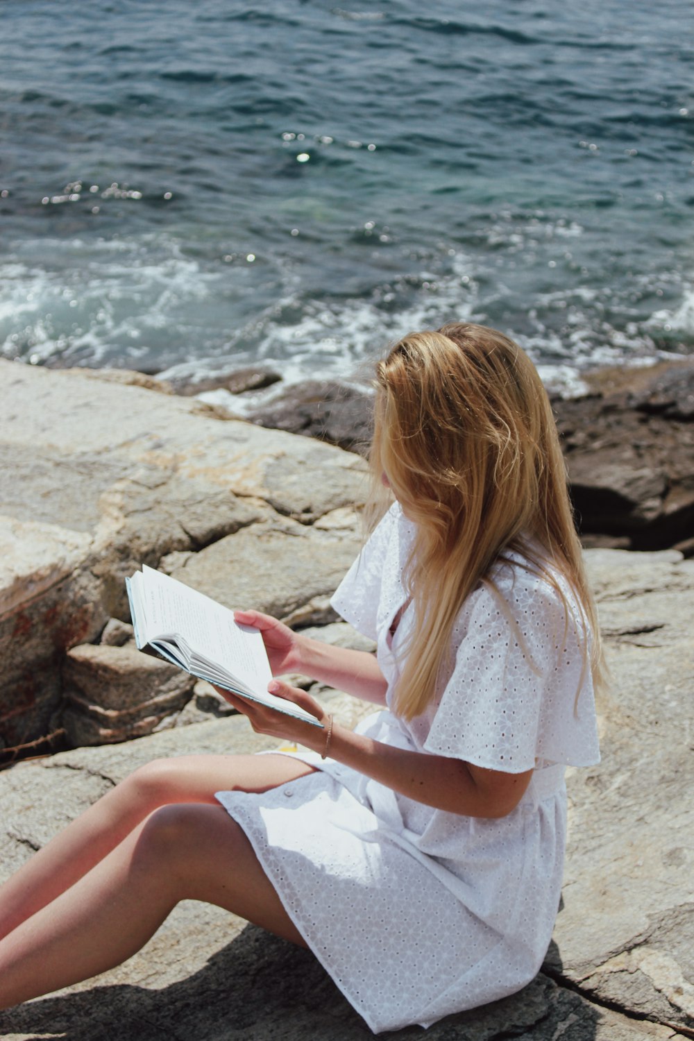 a woman sitting on a rock reading a book