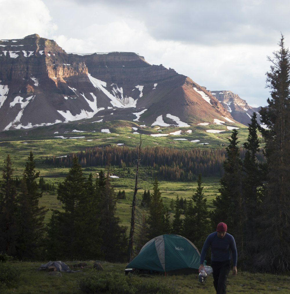 a man standing next to a tent on a lush green hillside