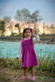 A little girl spinning happily in a bright pink dress outdoors.