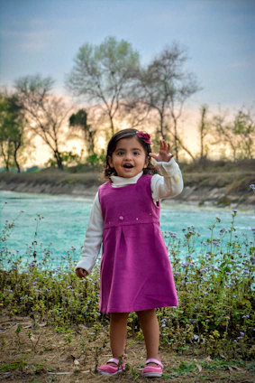 A smiling little girl dressed in a pastel pink dress with floral patterns, twirling in a garden.