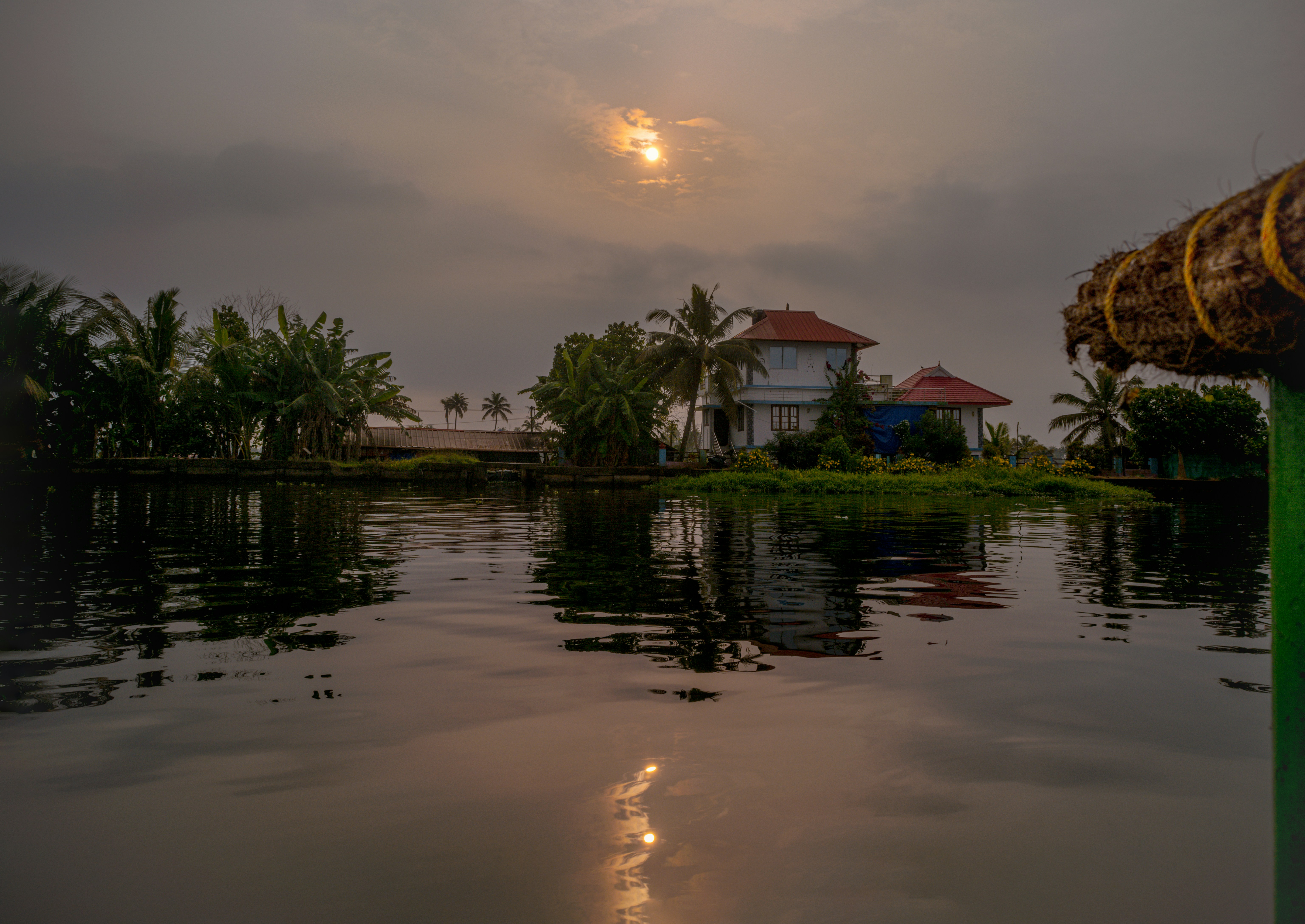 the sun is setting over a house on the water