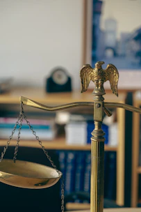 Close-up of golden legal scales on a dark wooden desk with law books in background.