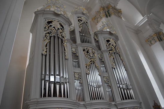 A grand pipe organ adorned with intricate gold and white detailing fills the space, emphasizing its impressive size. The metal pipes and ornate carvings are highlighted by the soft lighting of the surrounding architectural elements.