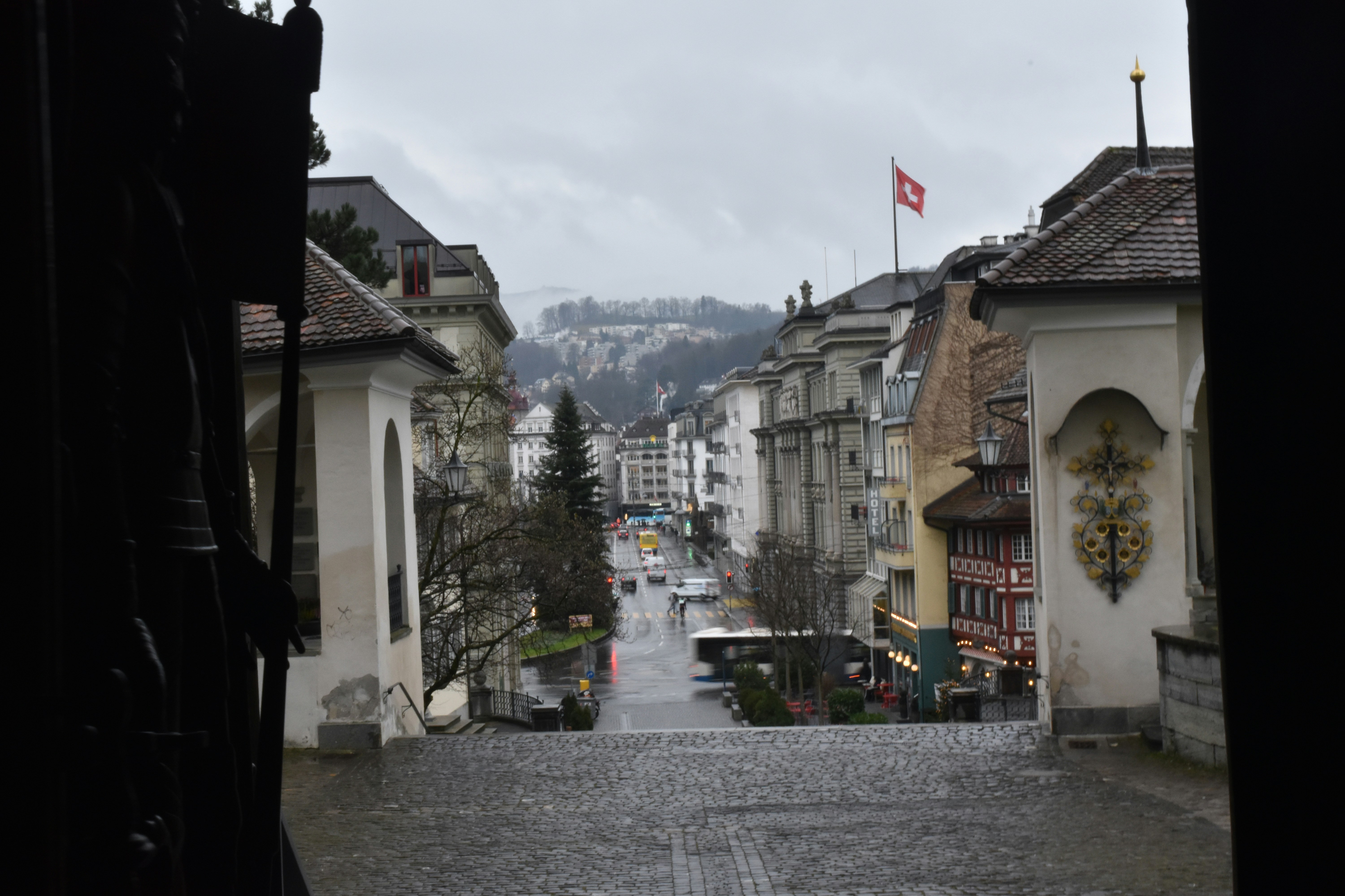 a cobblestone street with buildings and a flag on a hill in the background