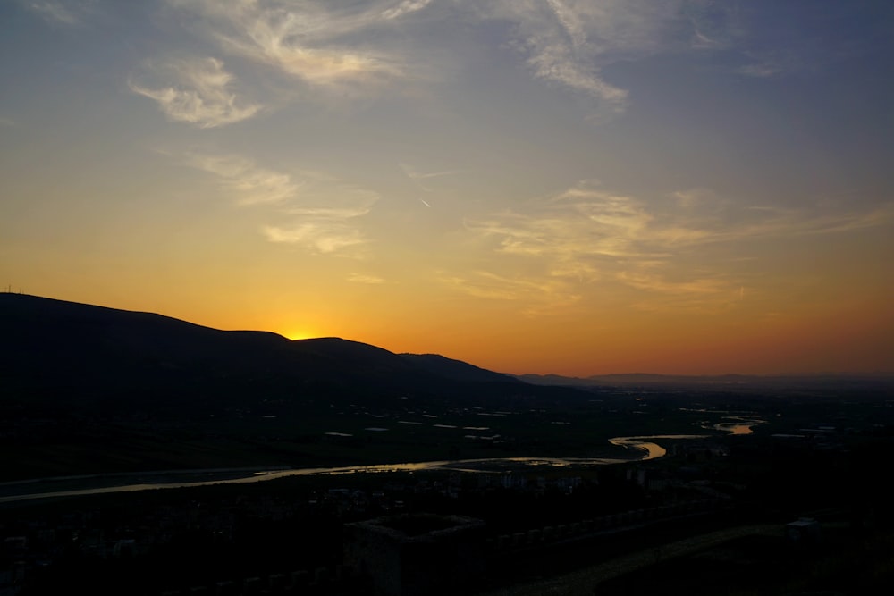 the sun is setting over the mountains and a river