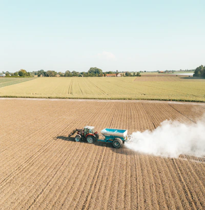 A farmer spreading fertilizer across a lush green field under a clear sky.