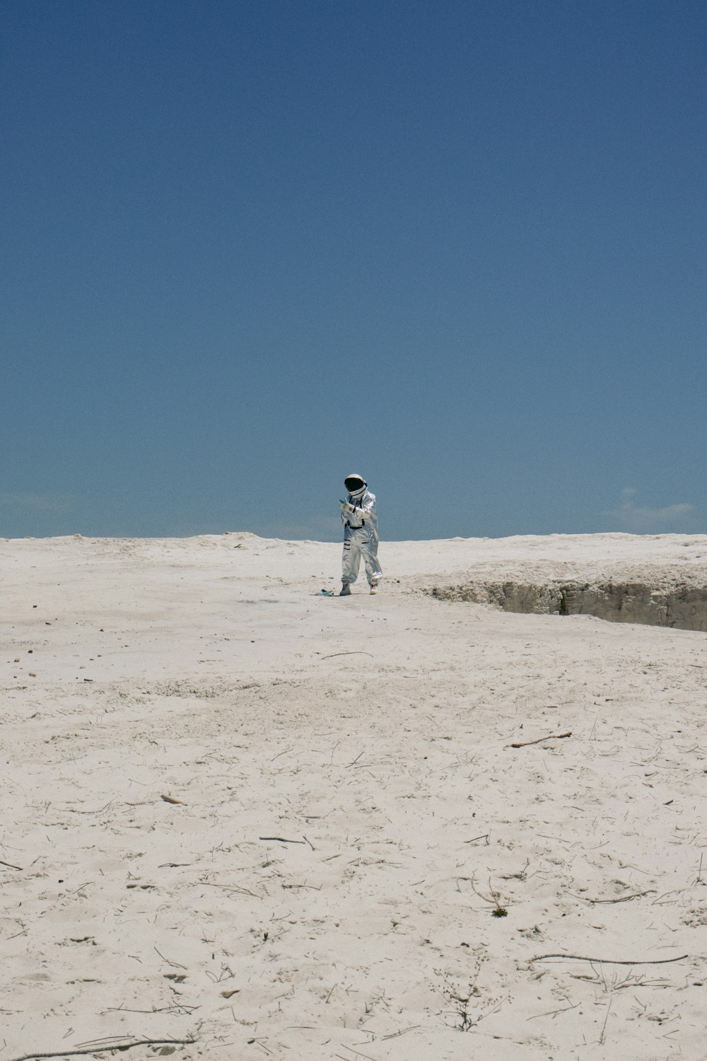 a man in a white space suit standing in the sand