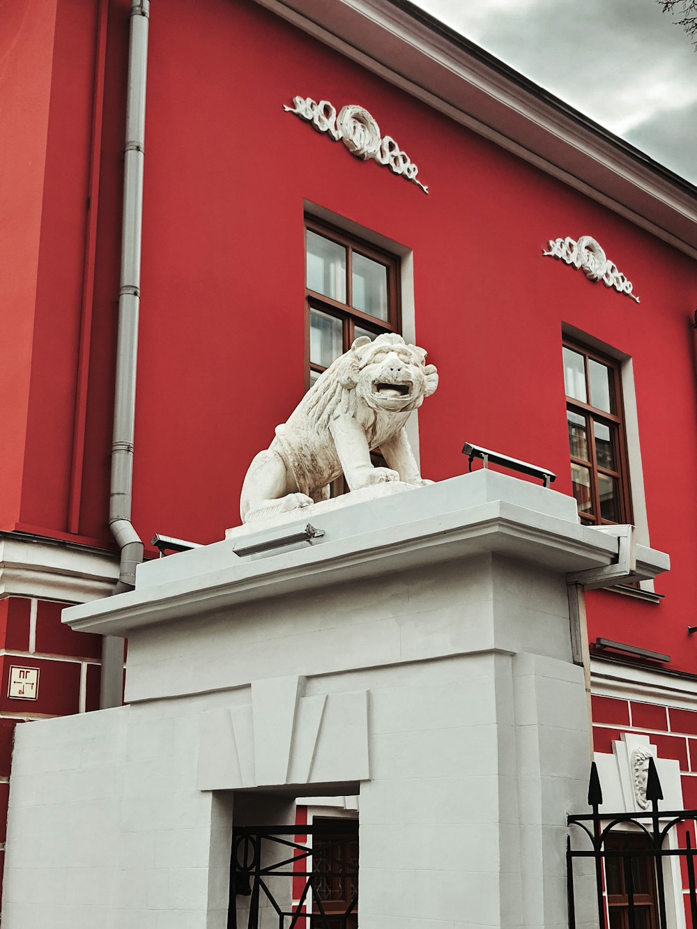 Una estatua de un león en un pedestal frente a un edificio rojo