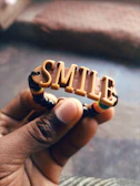 A smiling hand holding a cute charm with a small flower and heart design.