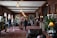 A plush, ornate interior with rich wooden paneling and vintage-style furniture. People are walking through a long corridor adorned with elegant lighting fixtures and elaborate floral arrangements. Large framed portraits line the walls, and the decor suggests an air of historic luxury. A classic car is partially visible to the left, adding to the ambiance.