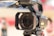 A professional 4K video camera is prominently featured, showcasing the lens with visible branding details. The camera appears mounted on a tripod, hinting at a setup for filming or photography. The background is blurred, emphasizing the camera as the focal point.