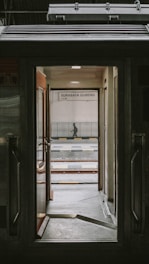 View through the open door of a train, revealing a platform with a sign that says 'Surabaya Gubeng'. The scene includes railway tracks and a person standing in the distance.