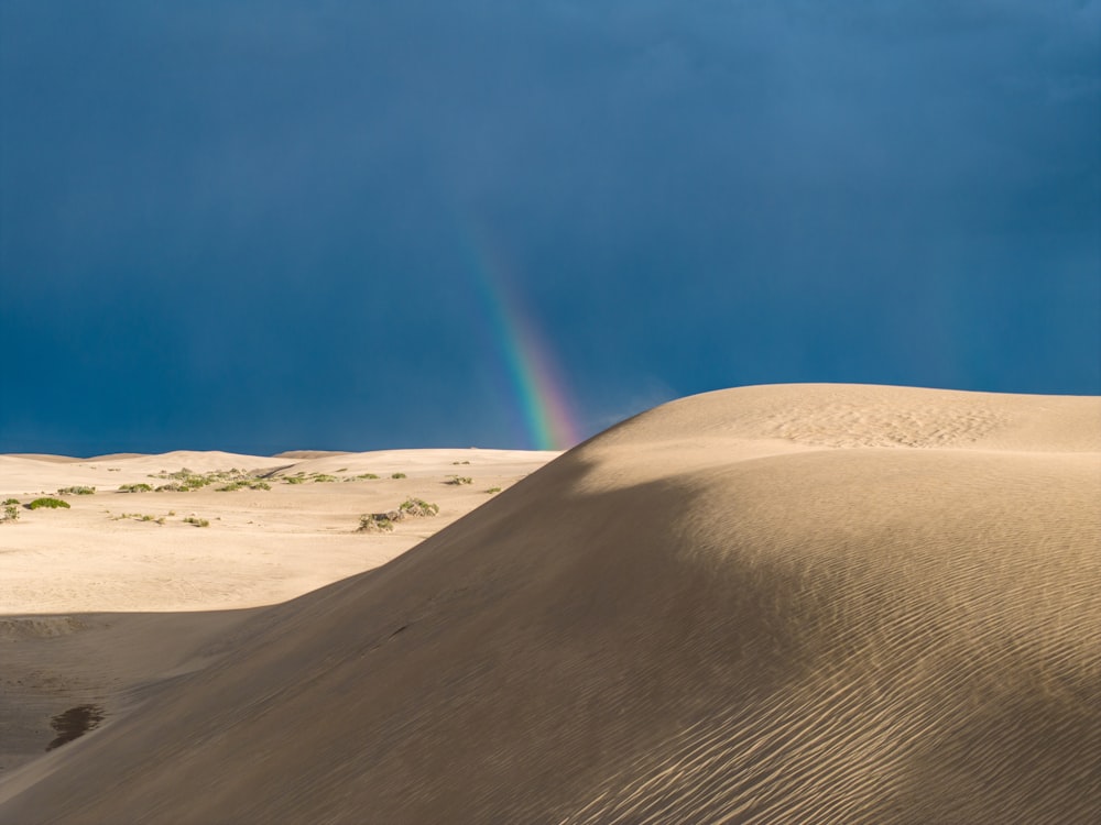 A rainbow shines in the sky over a sand dune photo – Free Desert Image on  Unsplash