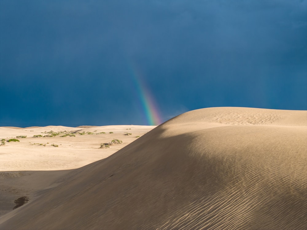 a rainbow shines in the sky over a sand dune
